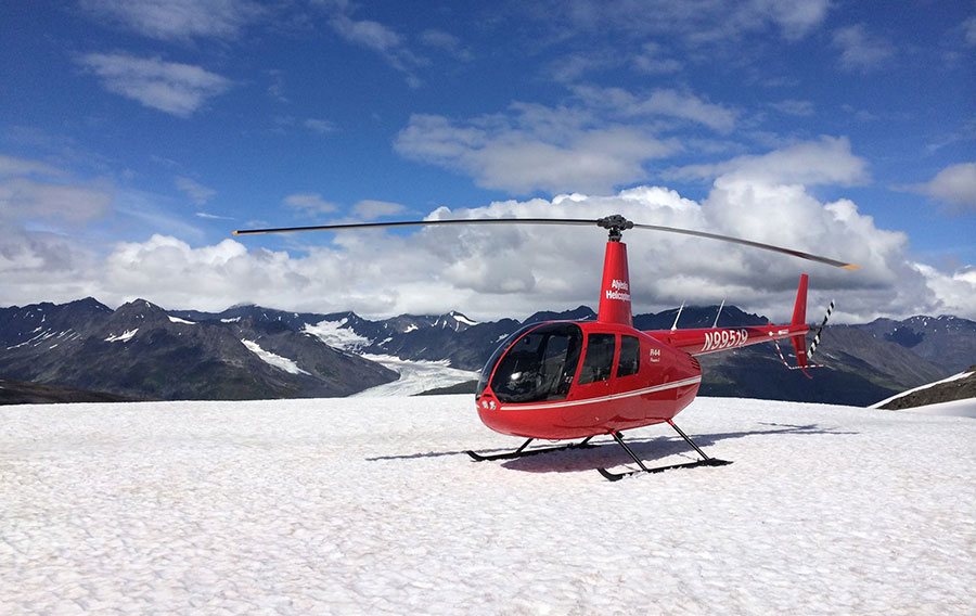 Helicopter landed on snowy field overlooking mountains and glacier.