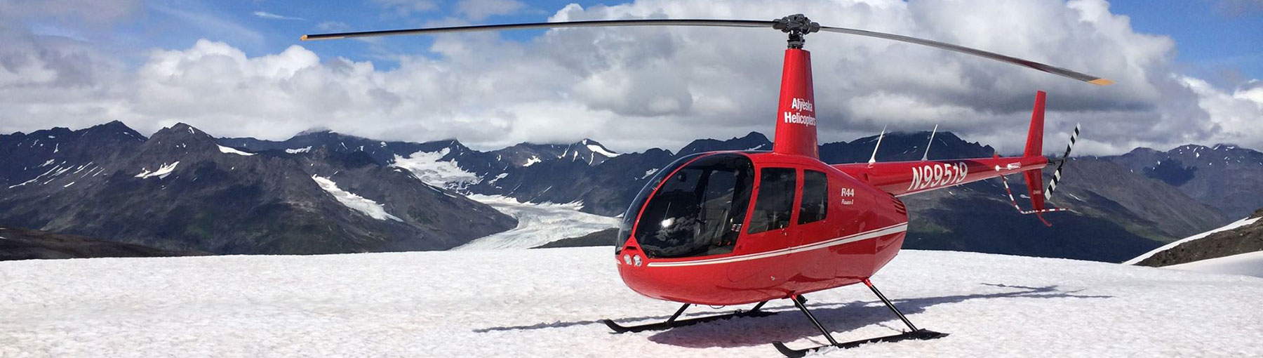 Helicopter landed on snowy field overlooking mountains and glacier.