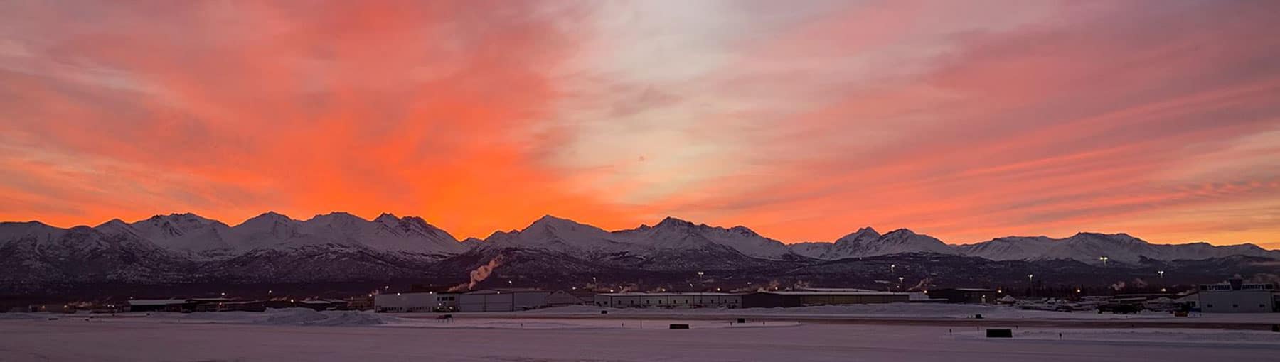 View of the airport with mountains and vibrant sunset in the background.
