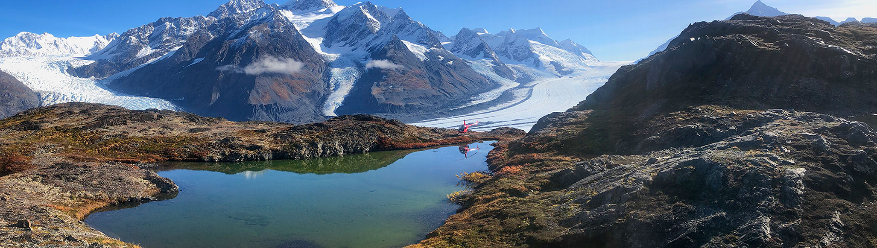 Ronbinson helicopter touched down next to beautiful Alaskan lake with snowy mountains and glacier in the background.