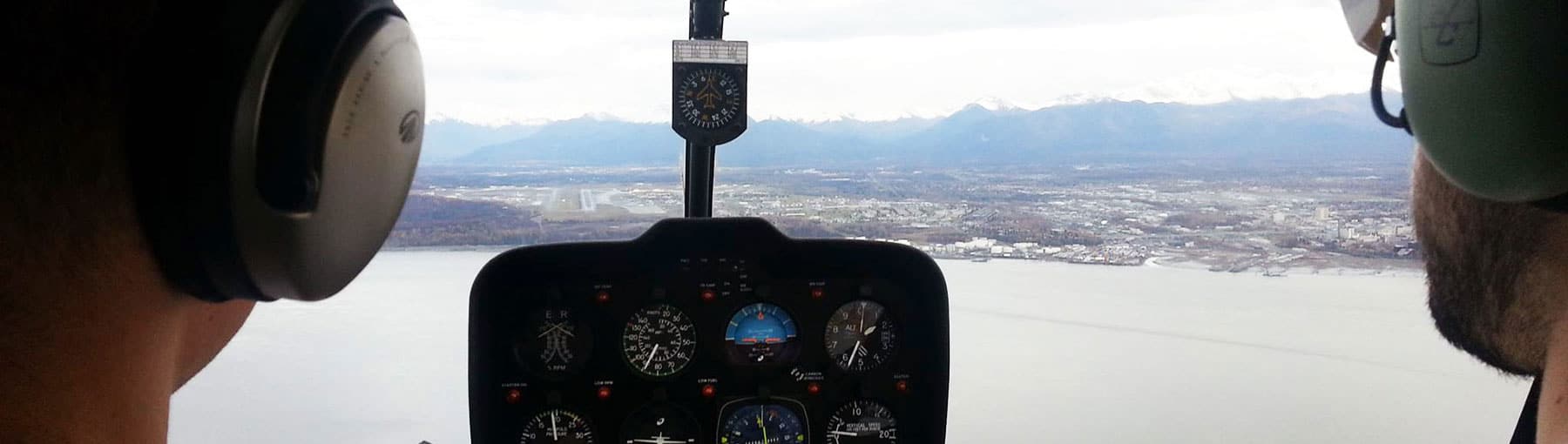 View of inside helicopter cockpit from behind two pilots with Anchorage below.