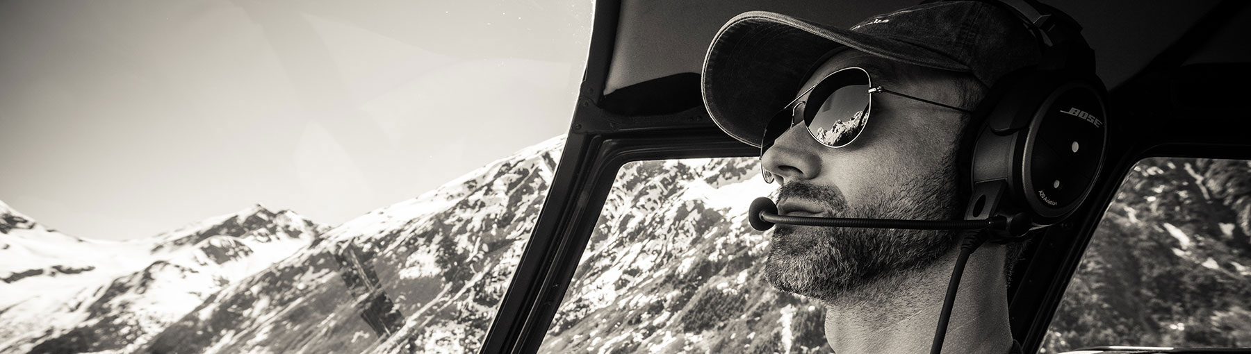 Helicopter pilot in the cockpit flying by snowy Alaskan mountains.