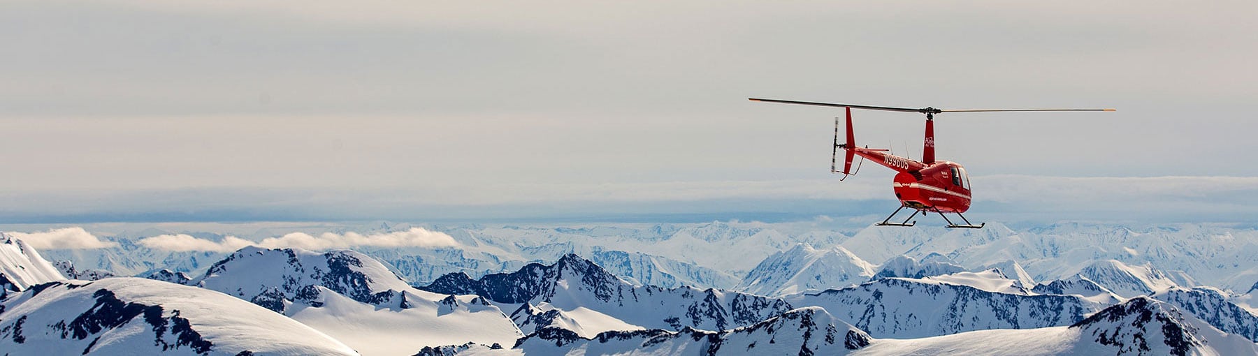Helicopter flying away towards snowy mountains.