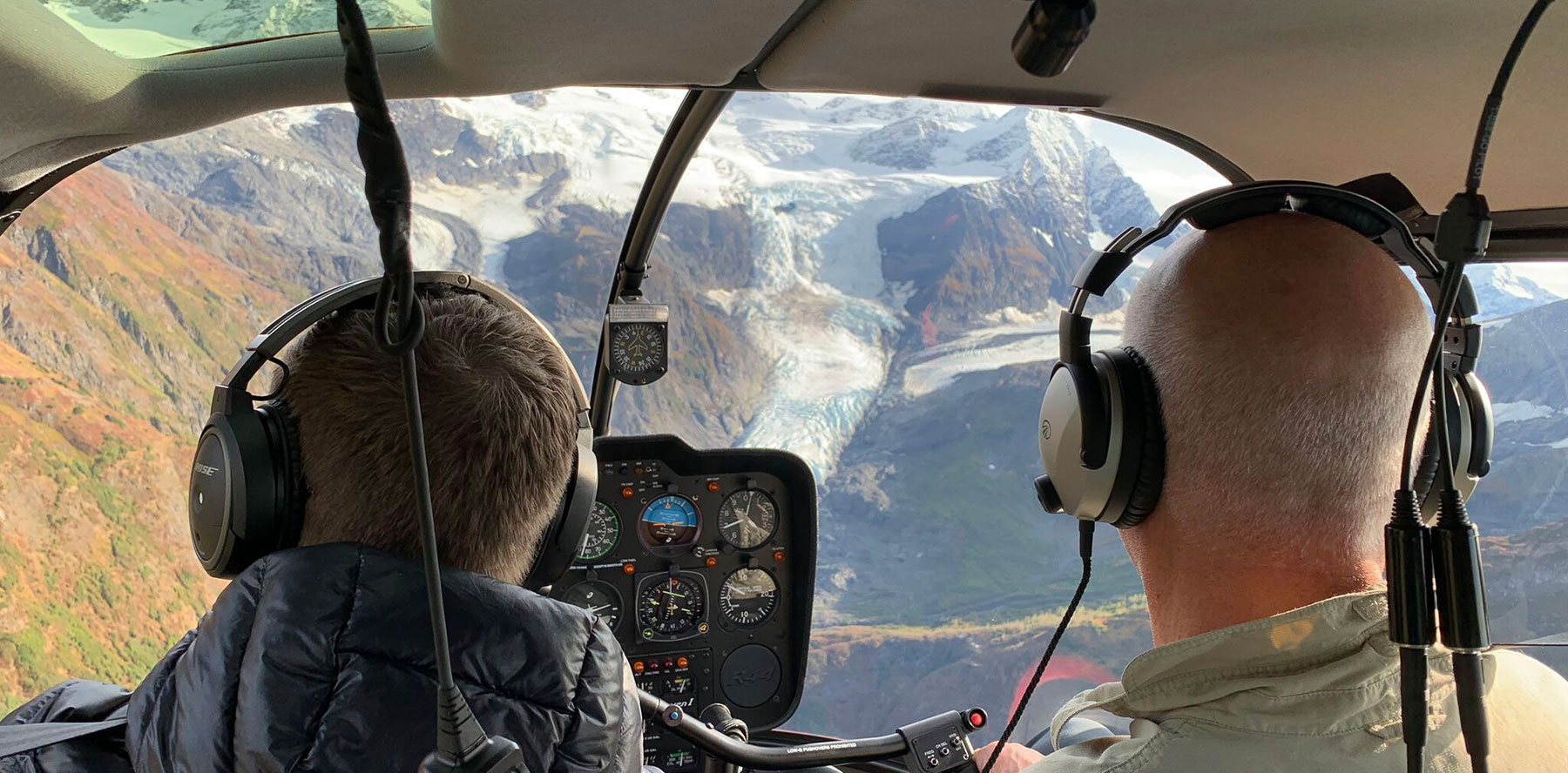 View of hanging glacier out of helicopter cockpit behind two pilots.