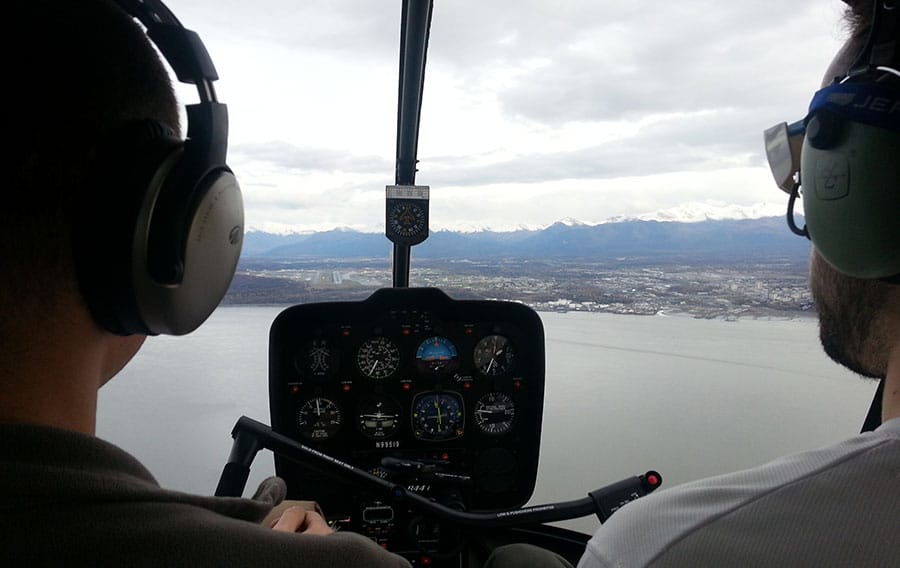 View of inside helicopter cockpit from behind two pilots with Anchorage below.